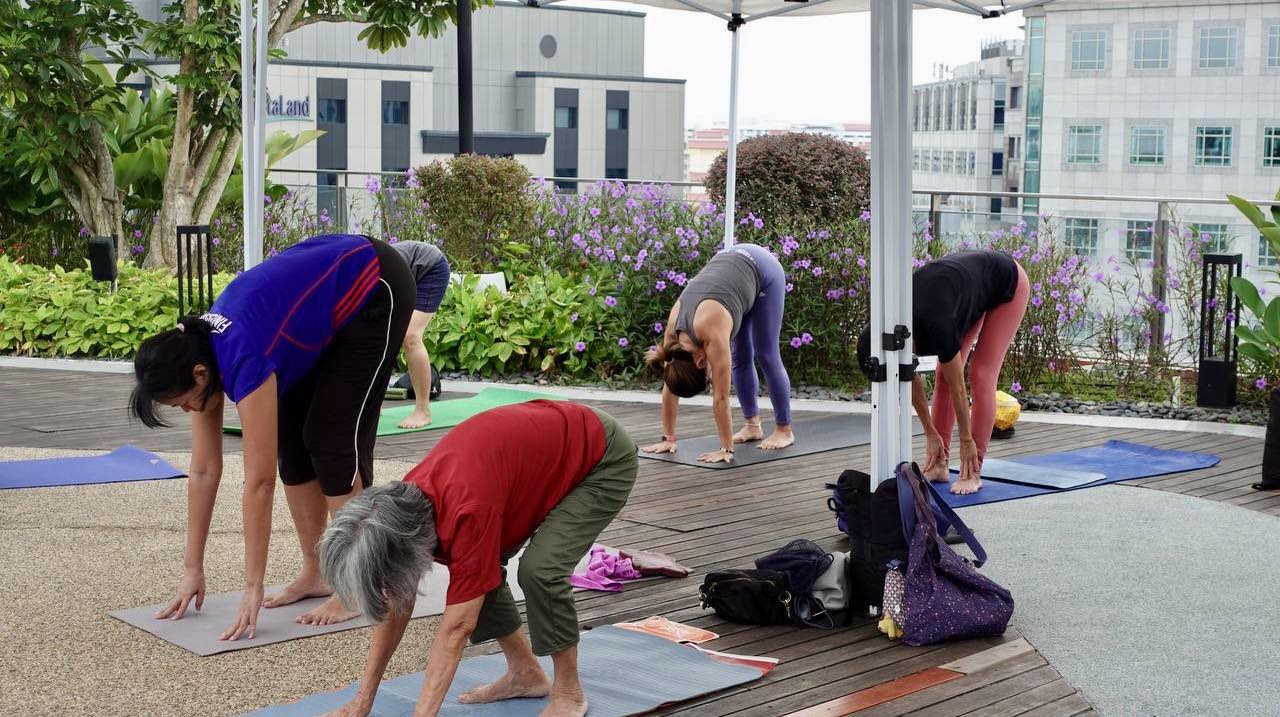 A yoga instructor guiding a group through a pose in a garden setting.