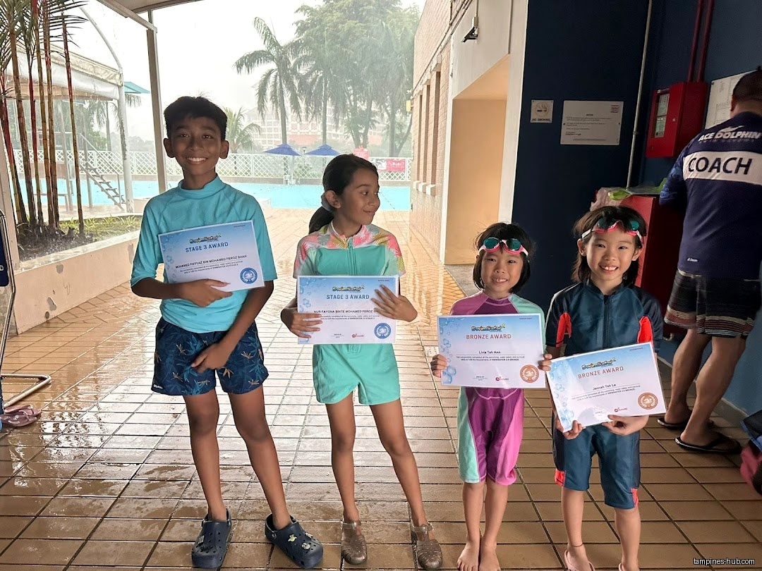 Four children in swimwear hold certificates at Ace Dolphin Swim School.