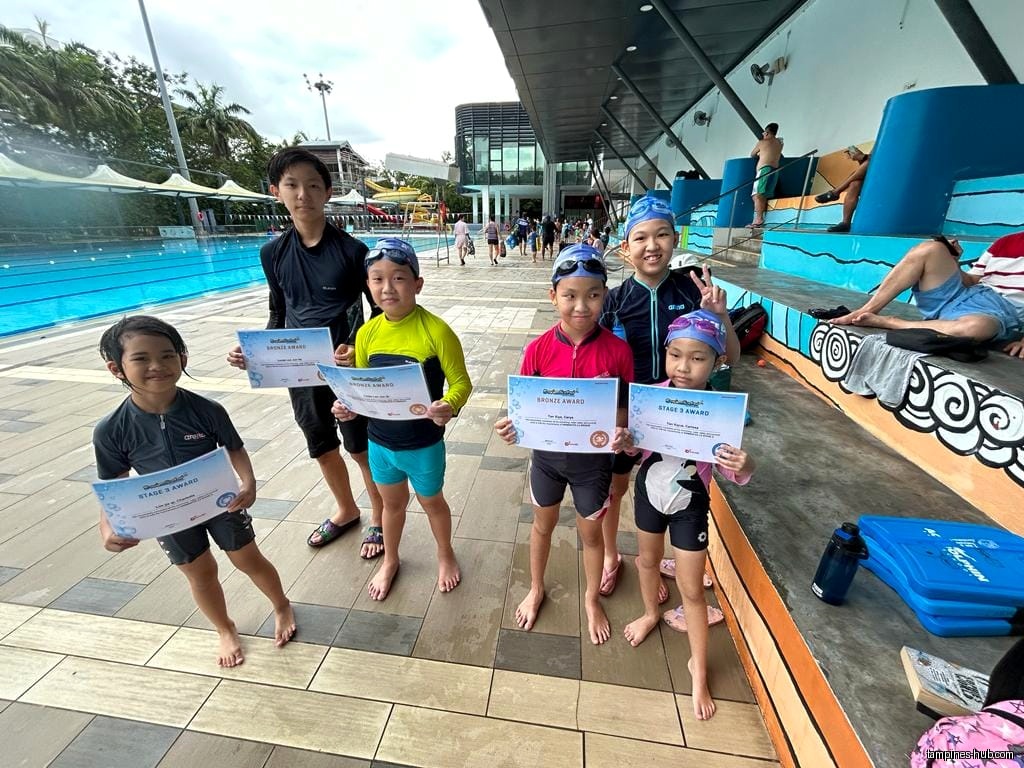 Children holding swimming awards at Ace Dolphin Swim School near a pool.