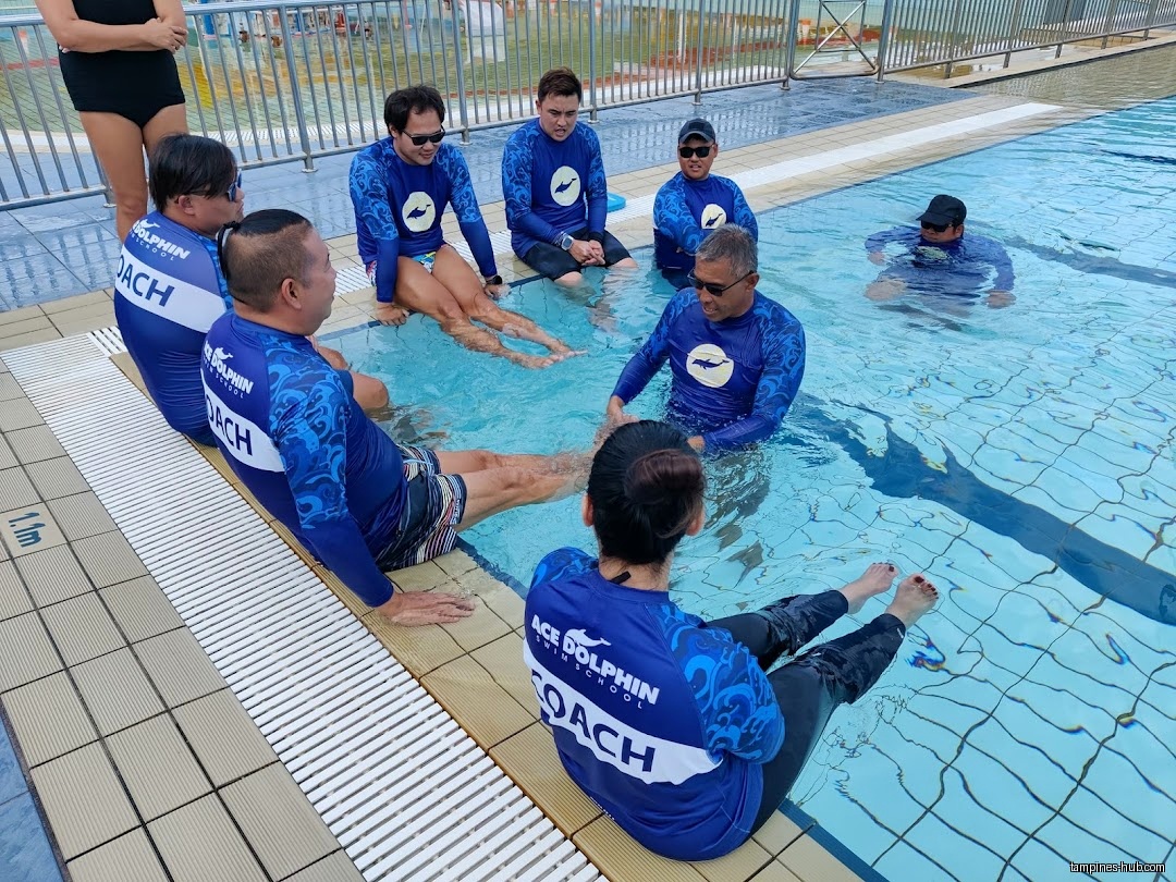 Swim coaches in matching shirts sit in and around a swimming pool.