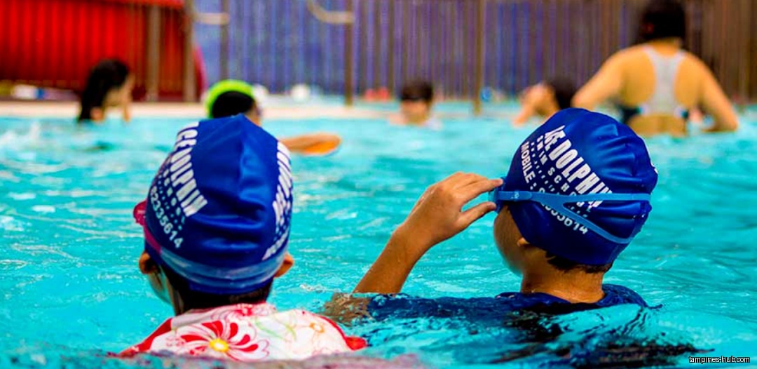 Children wearing swim caps swim in a pool at Ace Dolphin Swim School.