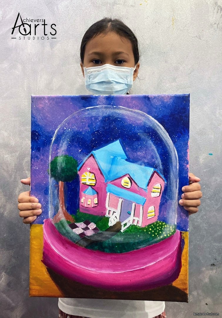 A child wearing a mask holds up a painting of a house.