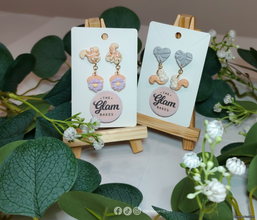 Two pairs of earrings on display stands, surrounded by floral decorations.