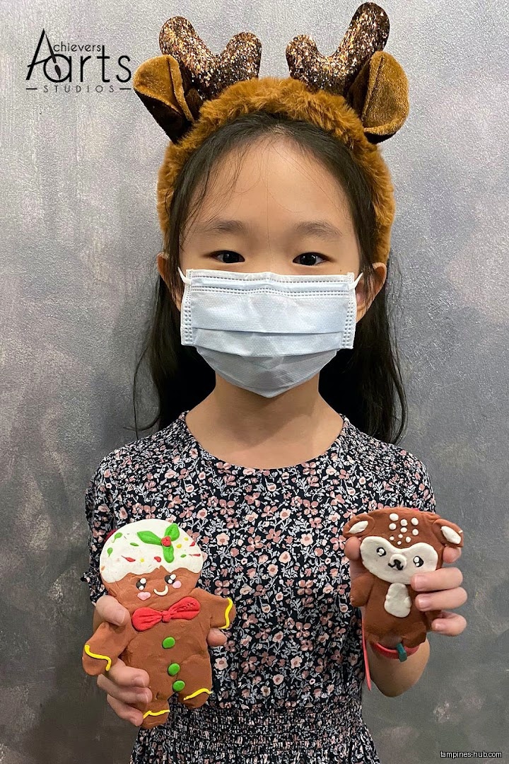 Girl wearing a mask and reindeer antlers holding Christmas-themed clay art.