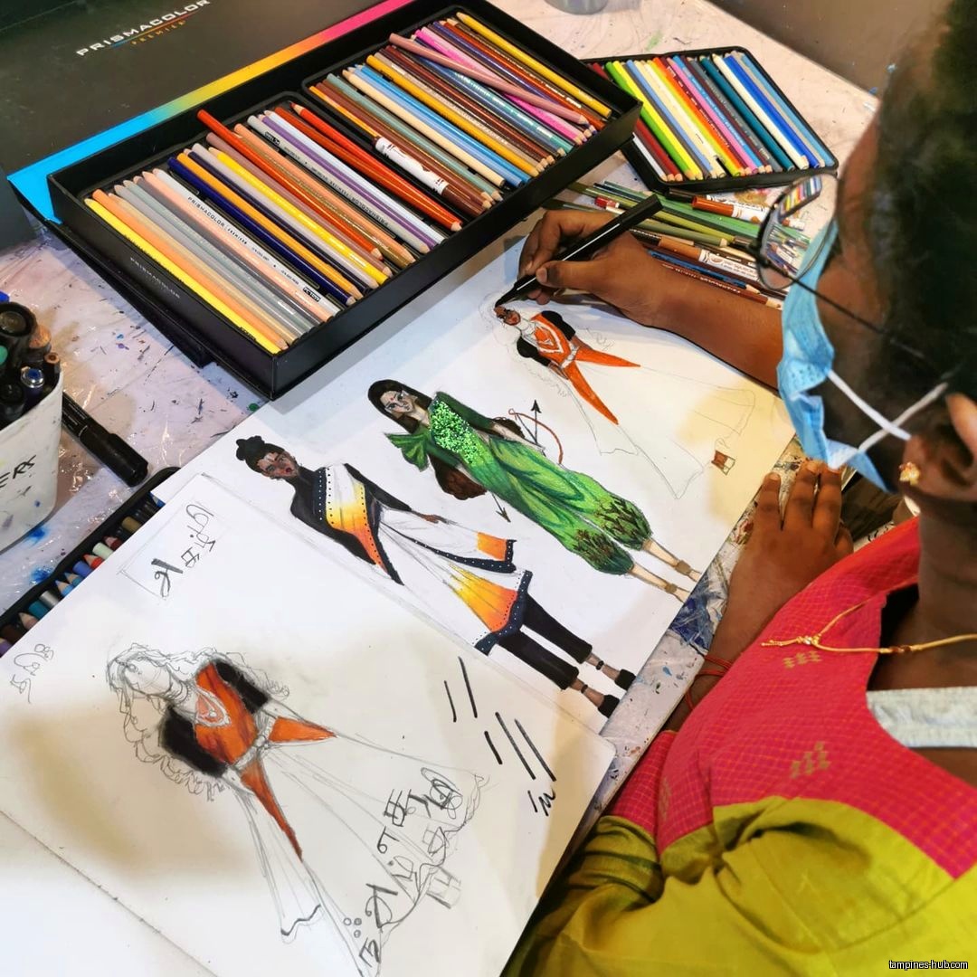 A person is drawing fashion designs with colored pencils and markers.