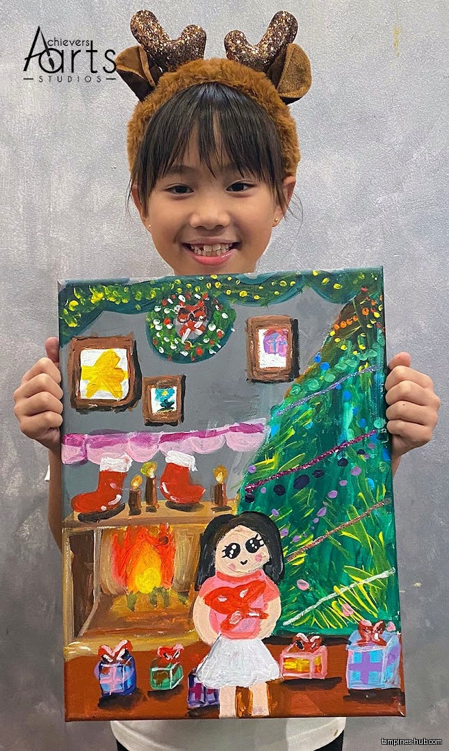 A girl holds up a Christmas-themed painting she created at Achievers Arts.