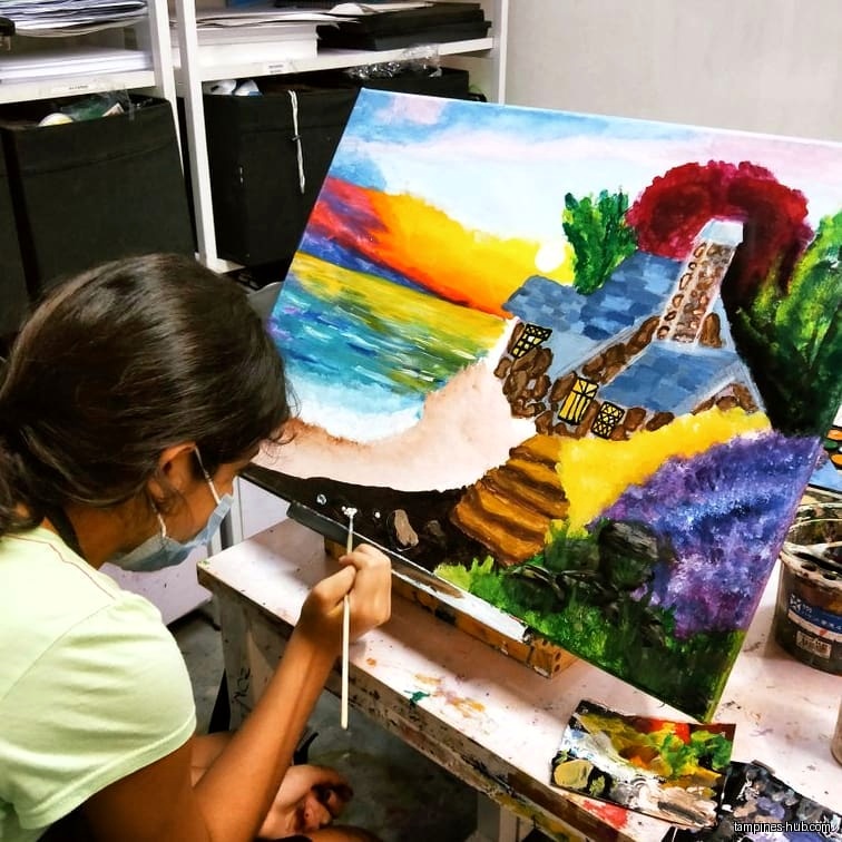 A person paints a landscape scene on a canvas in an art studio.