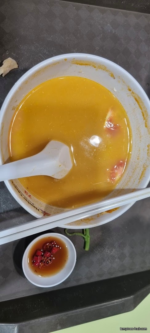A bowl of Ban Mian soup with a spoon and chili sauce.
