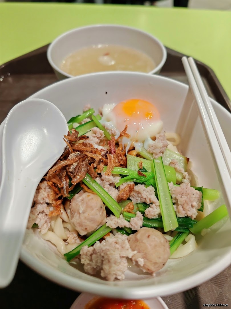 A bowl of Ban Mian with egg, vegetables, and soup on a tray.