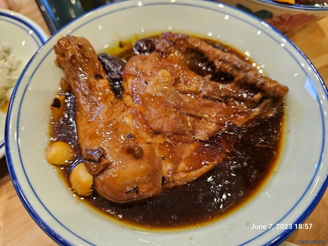 A plate of braised chicken with dark sauce and small potatoes.