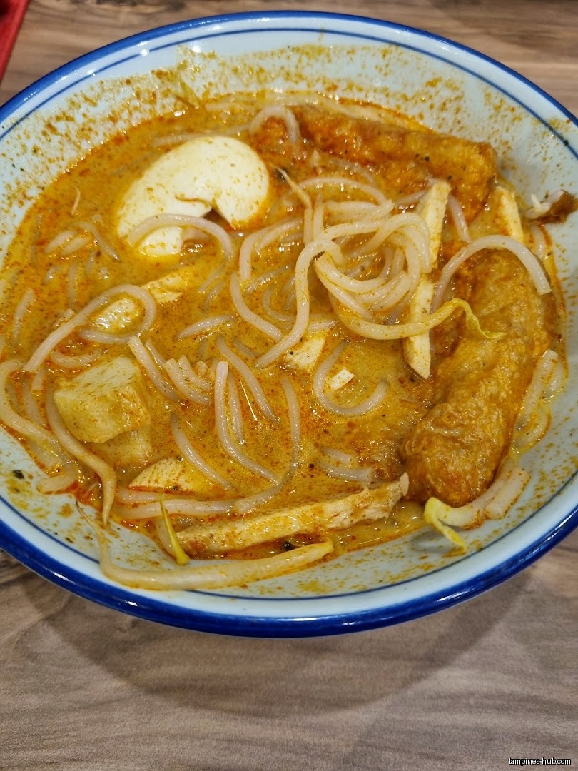 A bowl of Laksa with noodles, egg, and fried tofu.