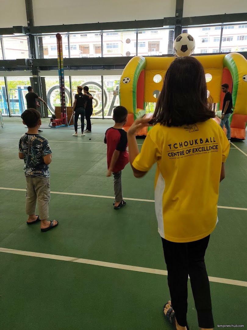 Children play games at an event, including a high striker and inflatable goal.