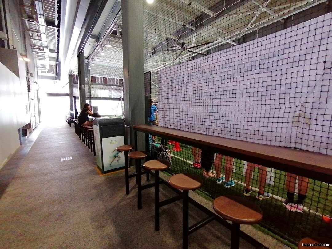 The image shows an indoor sports area with seating and netting.