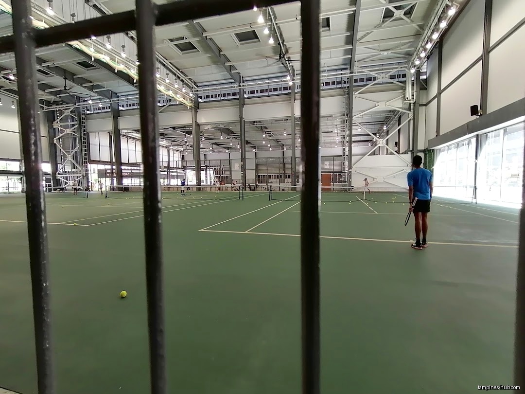 Indoor tennis court with players seen through a fence.