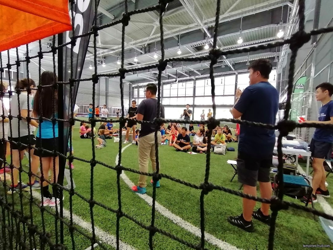 A group of people are gathered on an indoor turf field.