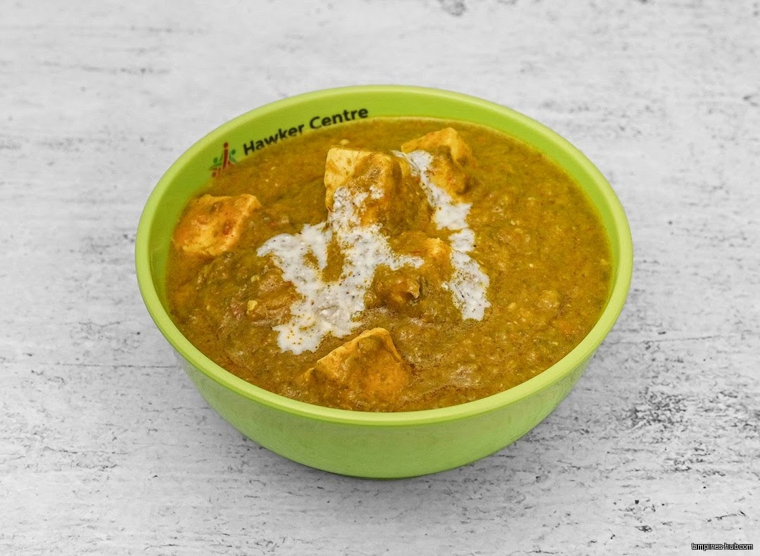 A green bowl filled with paneer butter masala and cream.