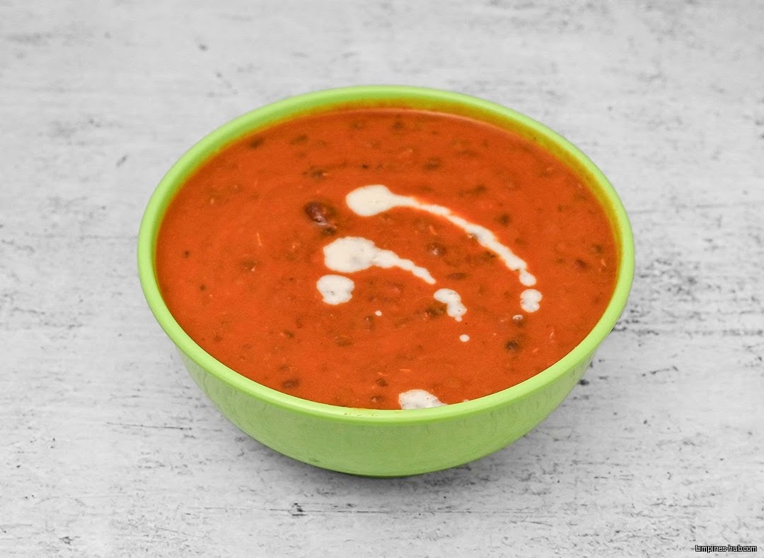 A bowl of dal makhani with cream on a white surface.