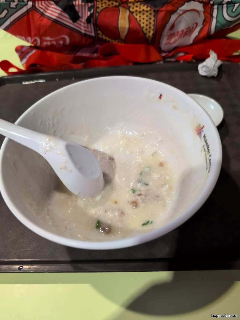 A bowl of partially eaten porridge with a spoon on a tray.