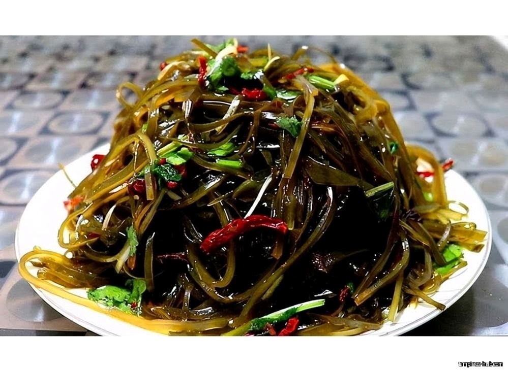 A plate of seaweed salad with chili peppers and herbs.