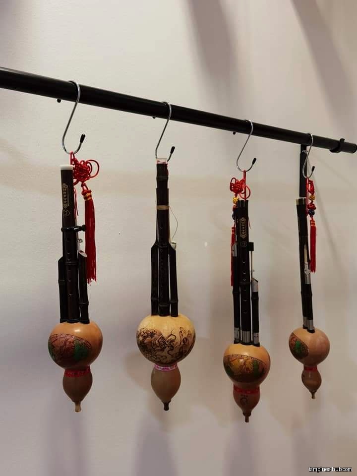 Four Chinese gourd flutes hang on a black metal bar with hooks.