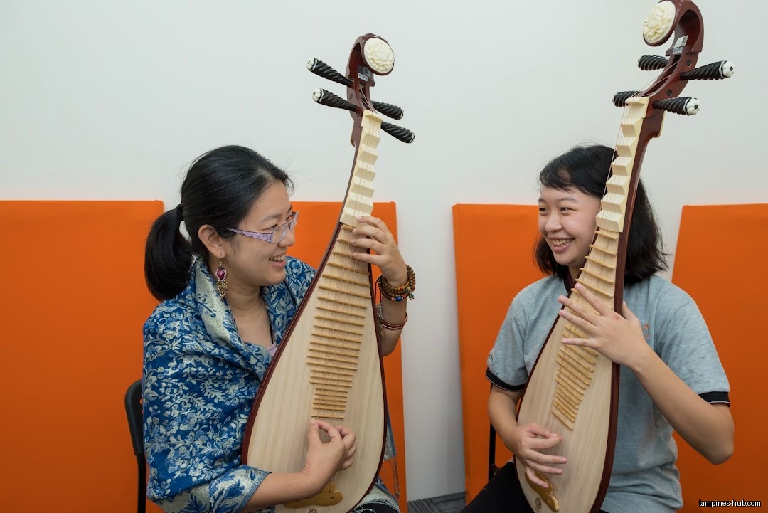 Two women smiling while holding and playing Chinese pipa instruments.
