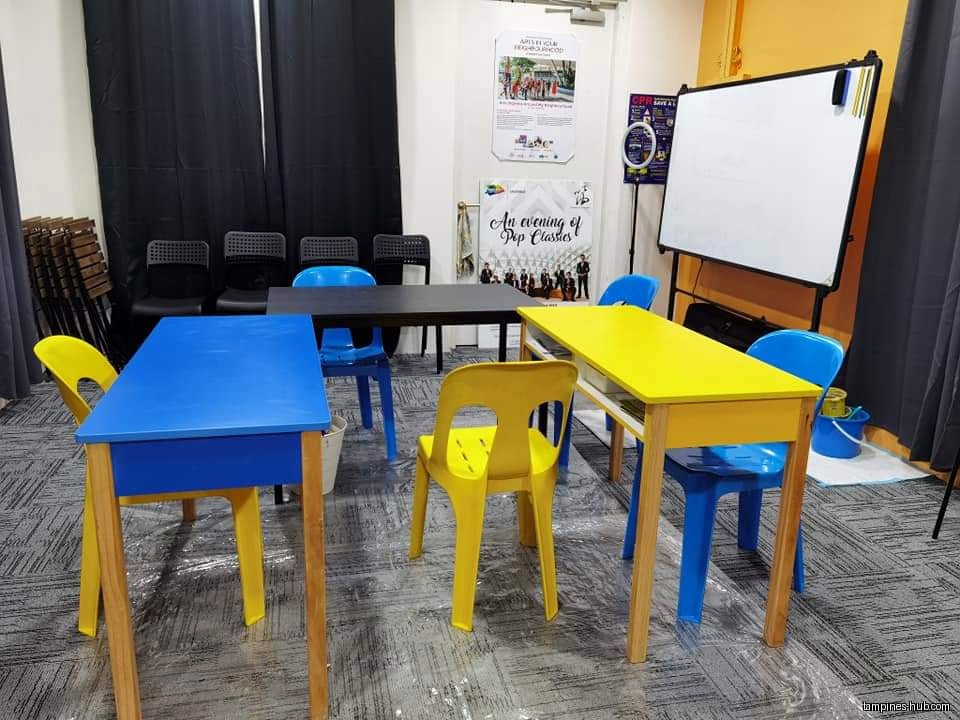 Classroom setting with colorful tables, chairs, and a whiteboard.
