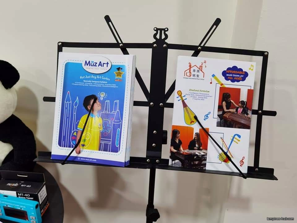 A music stand displays promotional materials for Muz Art and Chinese Instrumental Music School.