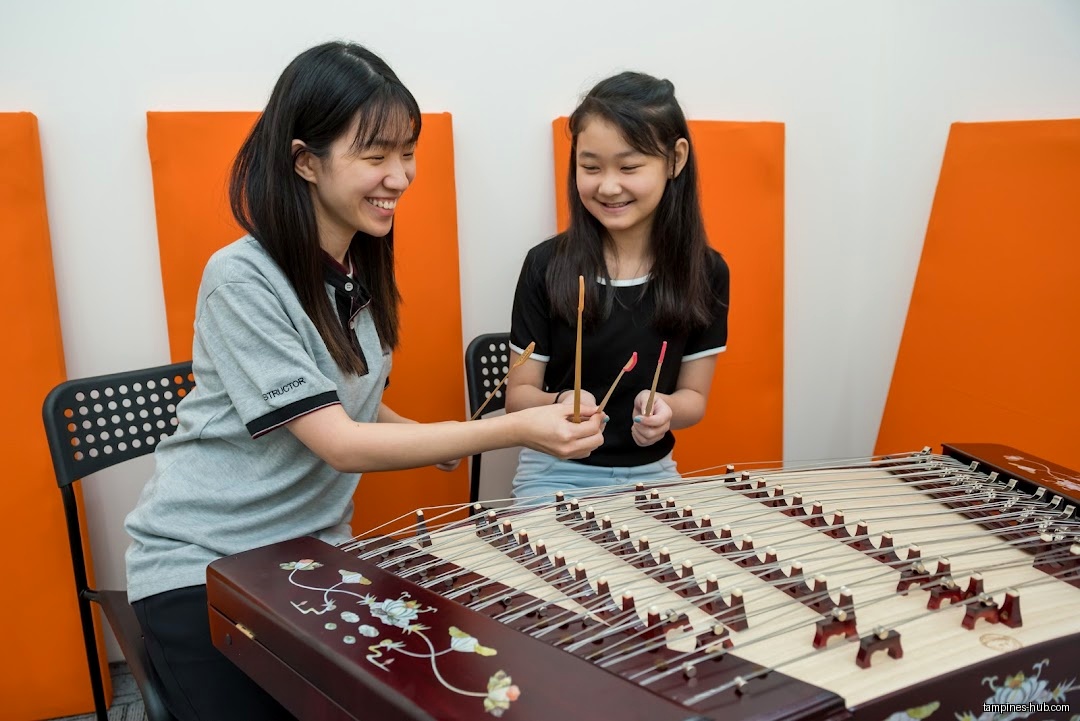 Two girls are playing a Chinese dulcimer with mallets in a room.