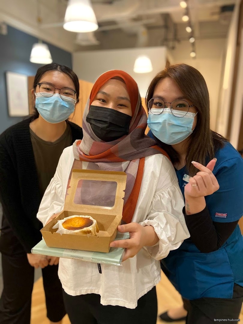 Three women wearing masks pose with a boxed dessert inside a shop.
