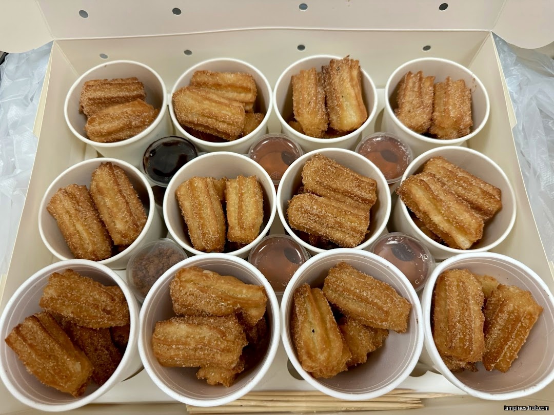A box of churros in cups with dipping sauces is displayed.