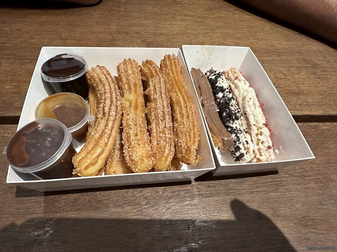 Two trays of churros with dipping sauces on a wooden table.