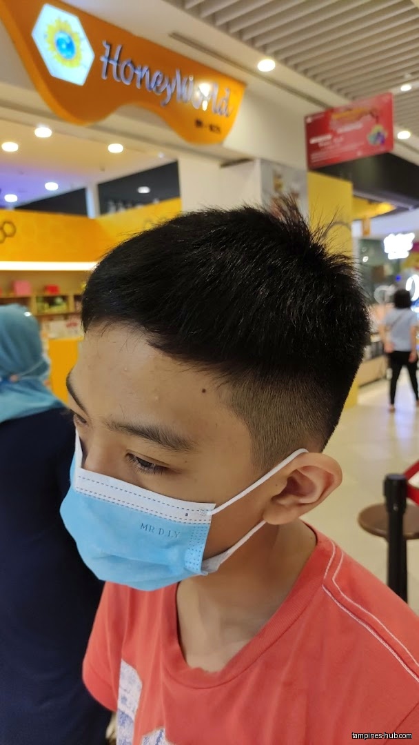 A boy wearing a mask with a fresh haircut in a mall.