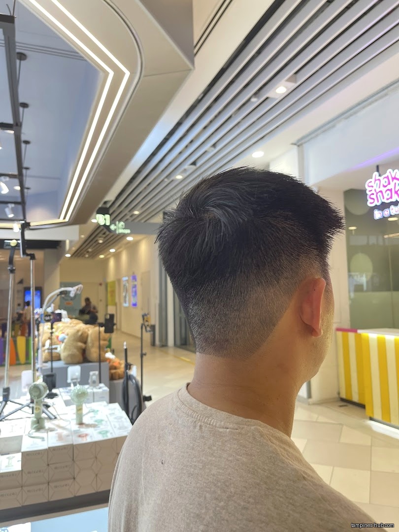 A man with a fresh haircut stands inside a shopping mall.