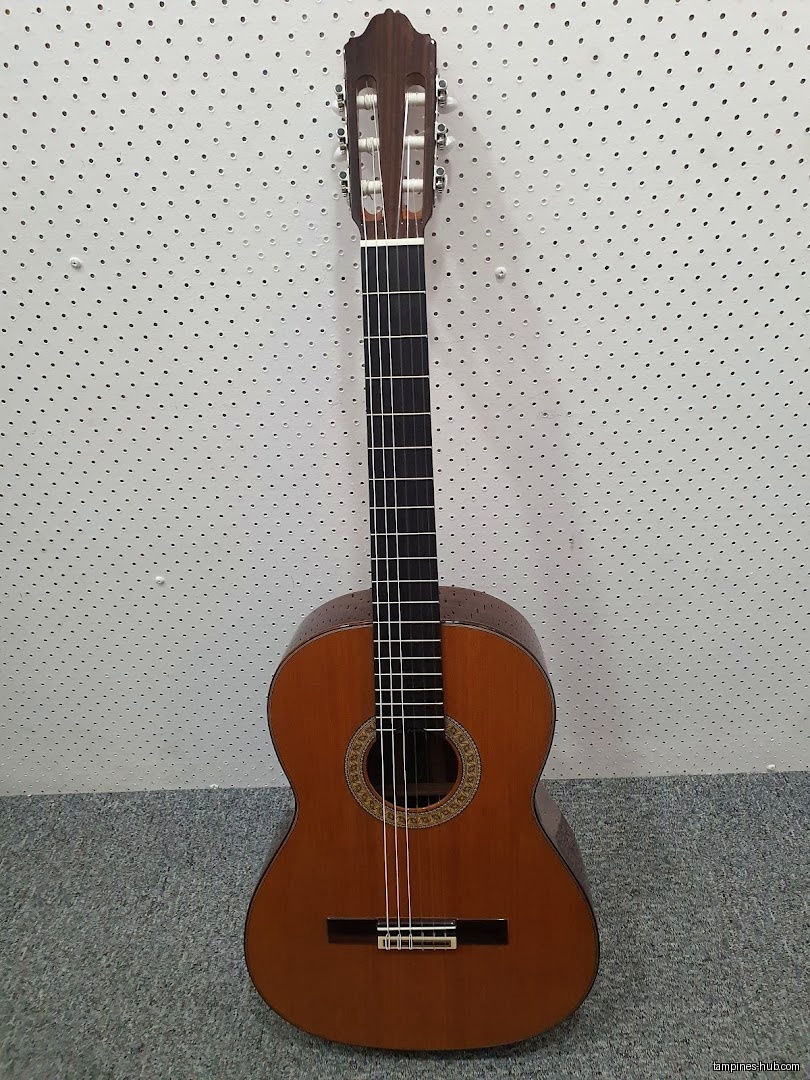 Acoustic guitar standing against a white wall with a gray floor.