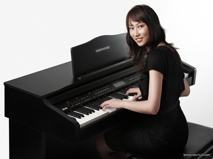 A woman plays a black Cristofori digital piano, smiling at the camera.