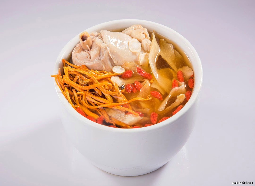 A bowl of herbal soup with chicken, goji berries, and other ingredients.