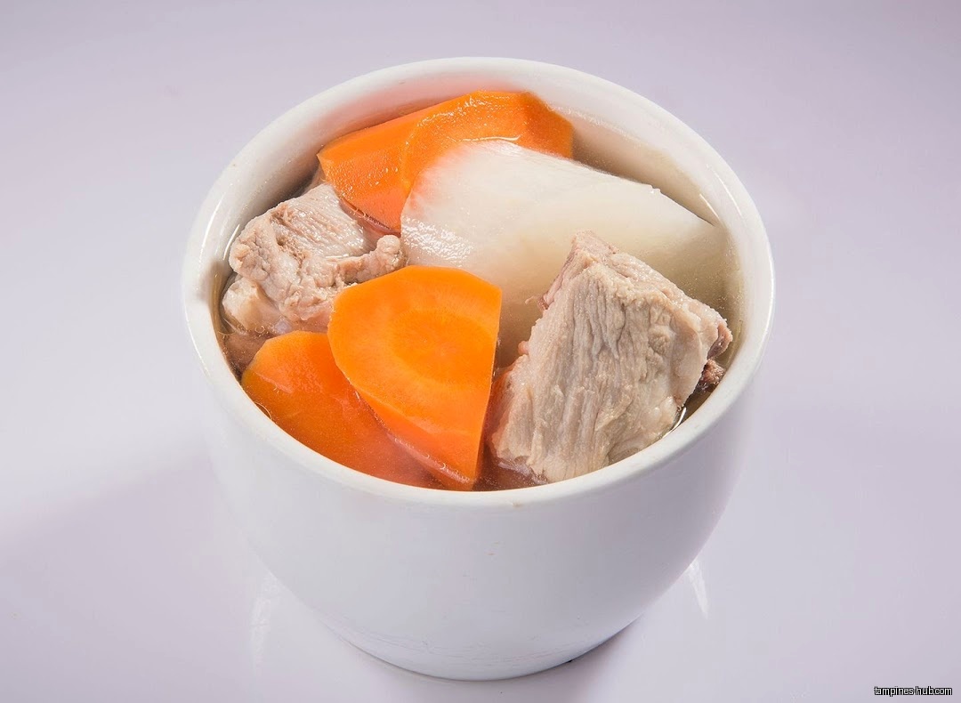 A bowl of herbal soup with carrots, radish, and meat.