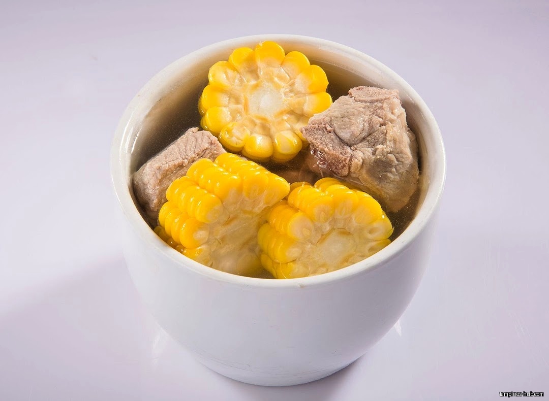 A white bowl filled with corn and meat in a clear broth.