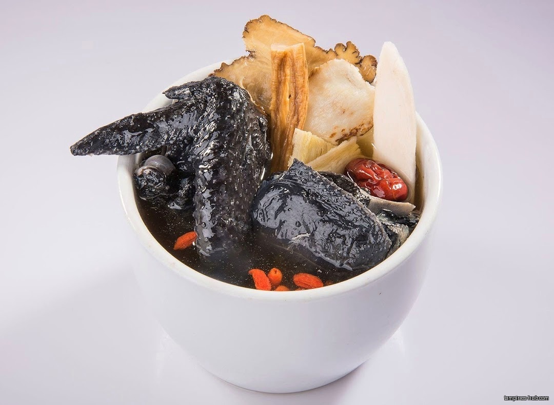 A bowl of black chicken herbal soup with various ingredients.