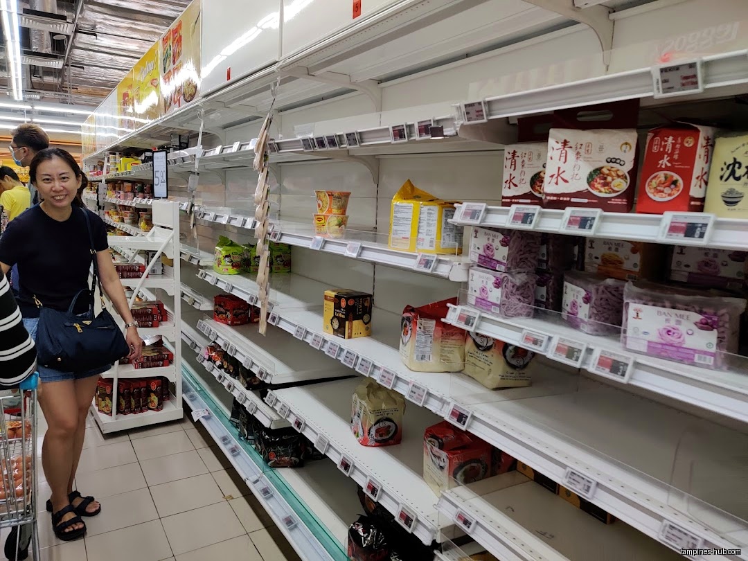 A woman shops in a FairPrice aisle with partially empty shelves.