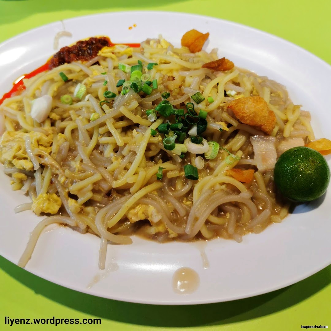 A plate of noodles with egg, green onions, chili, and a lime.