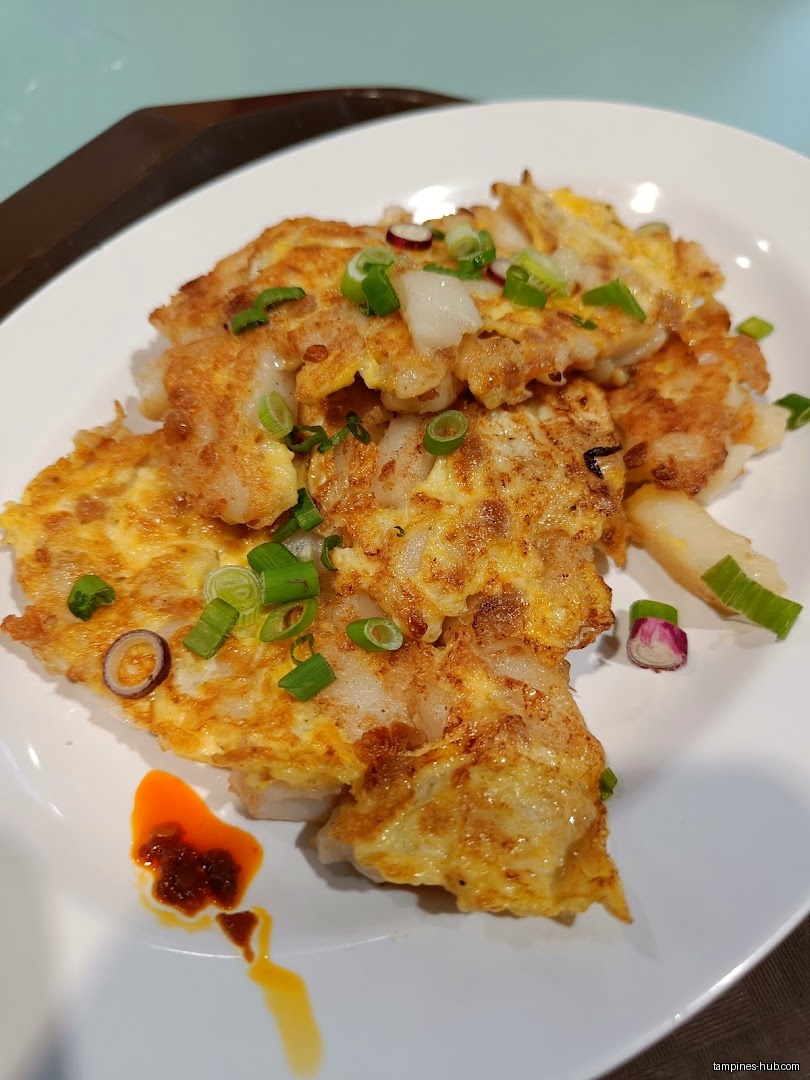 A plate of fried carrot cake with chili and green onions.