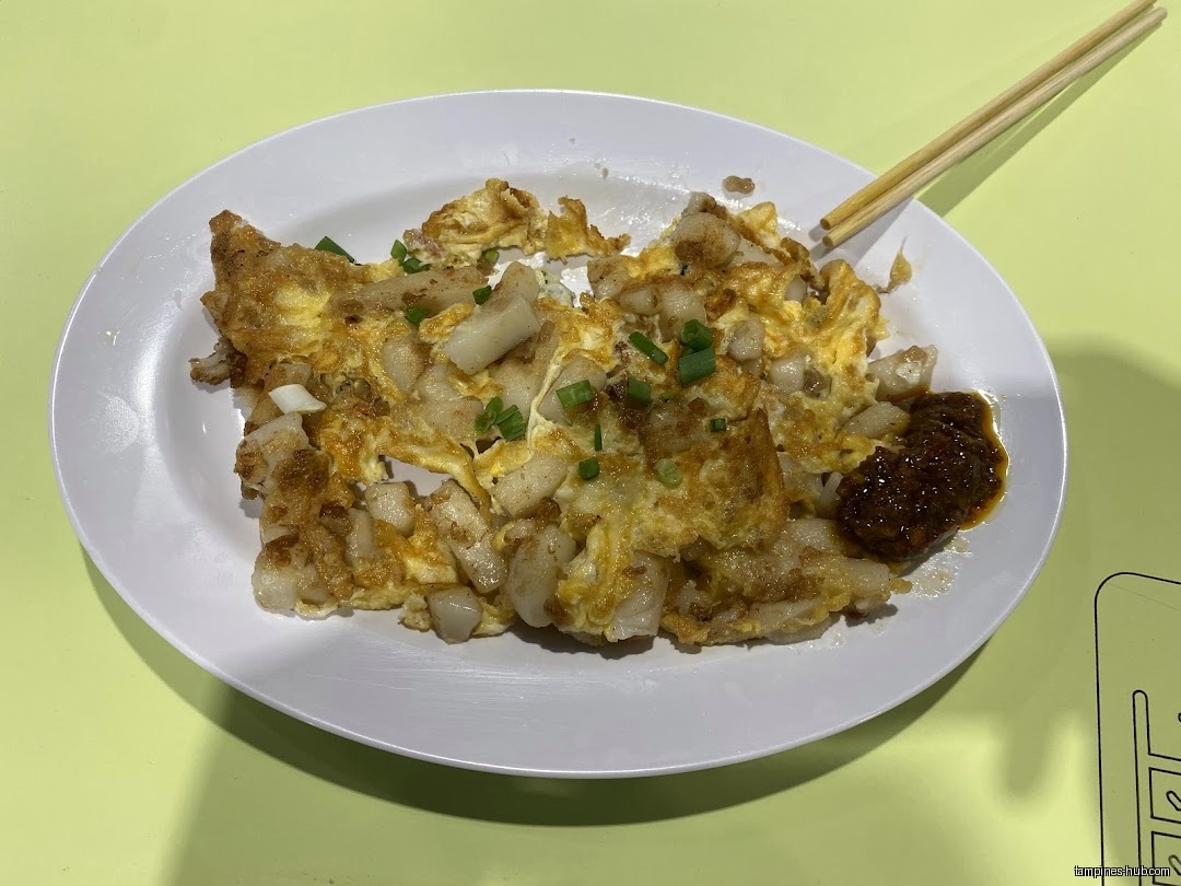A plate of fried carrot cake with chili and chopsticks is shown.