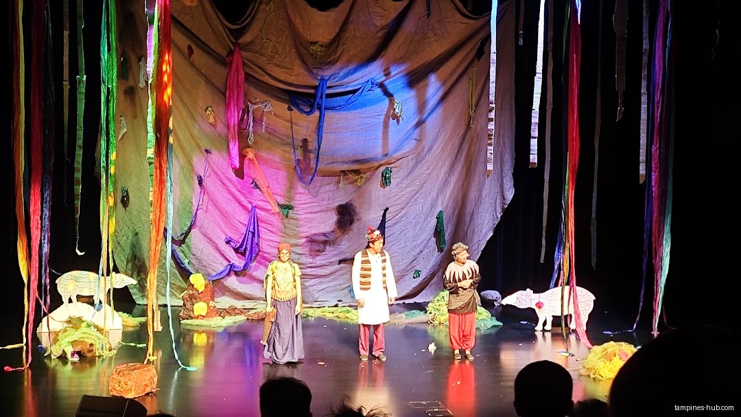 A stage performance with three actors and colorful set design is shown.