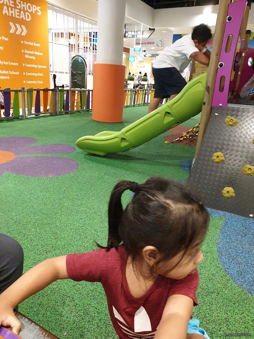 Children play on a slide and climbing wall in a play area.