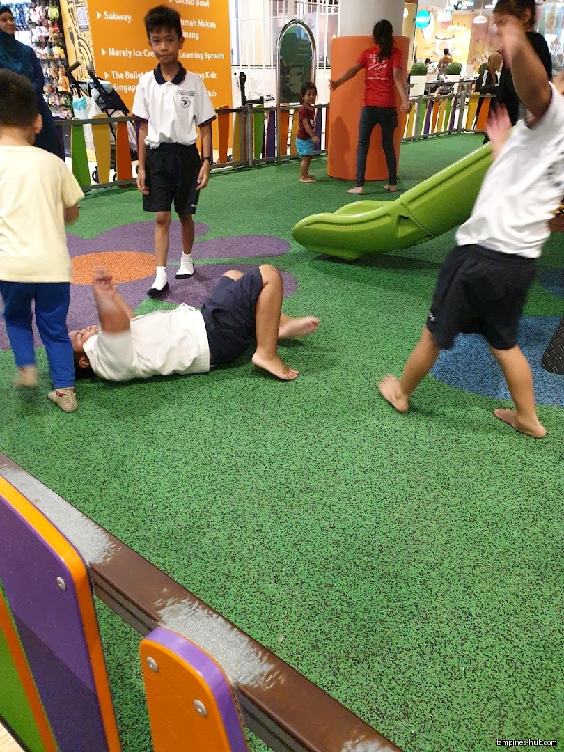 Children play on a green play area with a slide and colorful seating.