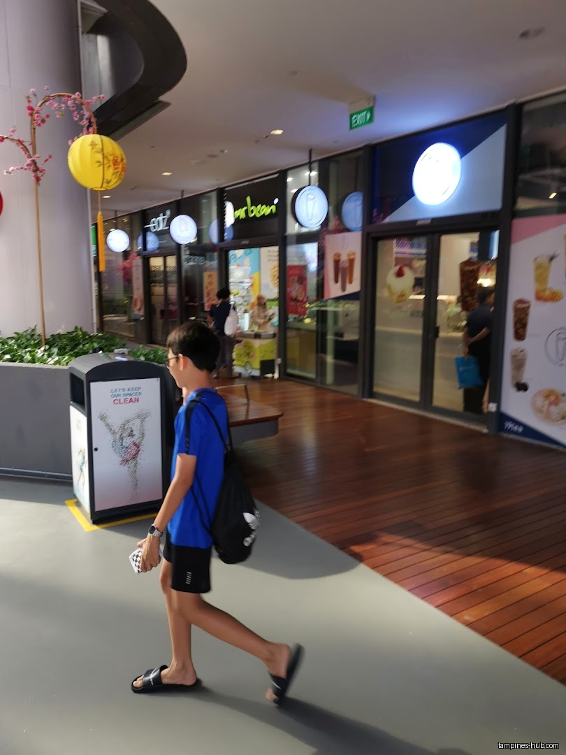 A boy walks past several shop fronts in a mall.