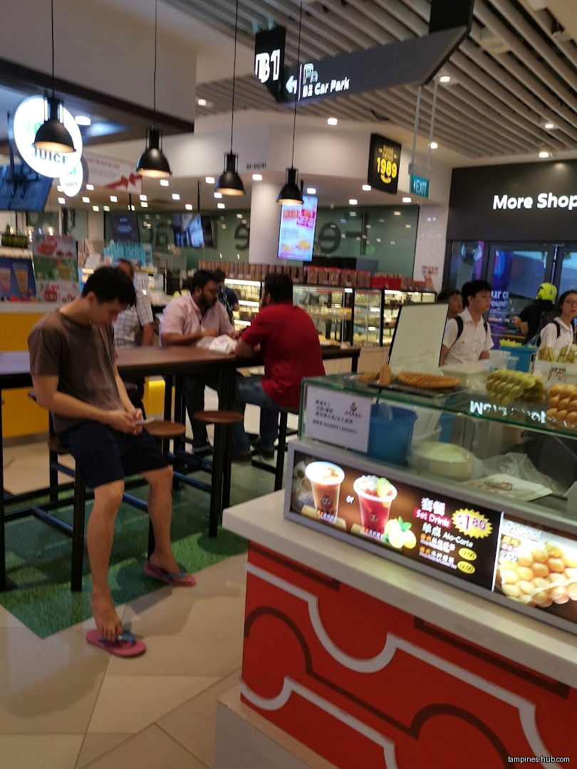People sit at tables near a food display in a shopping center.