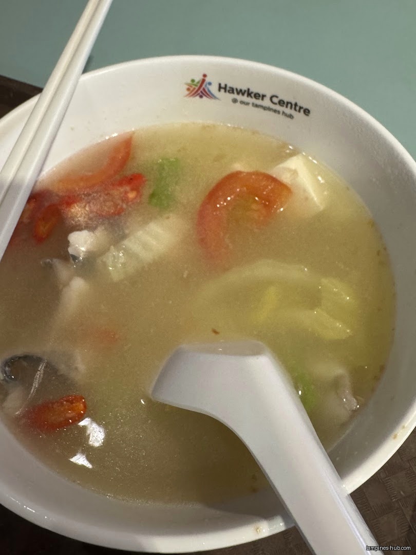 A bowl of fish soup with vegetables, tomatoes, and a spoon.