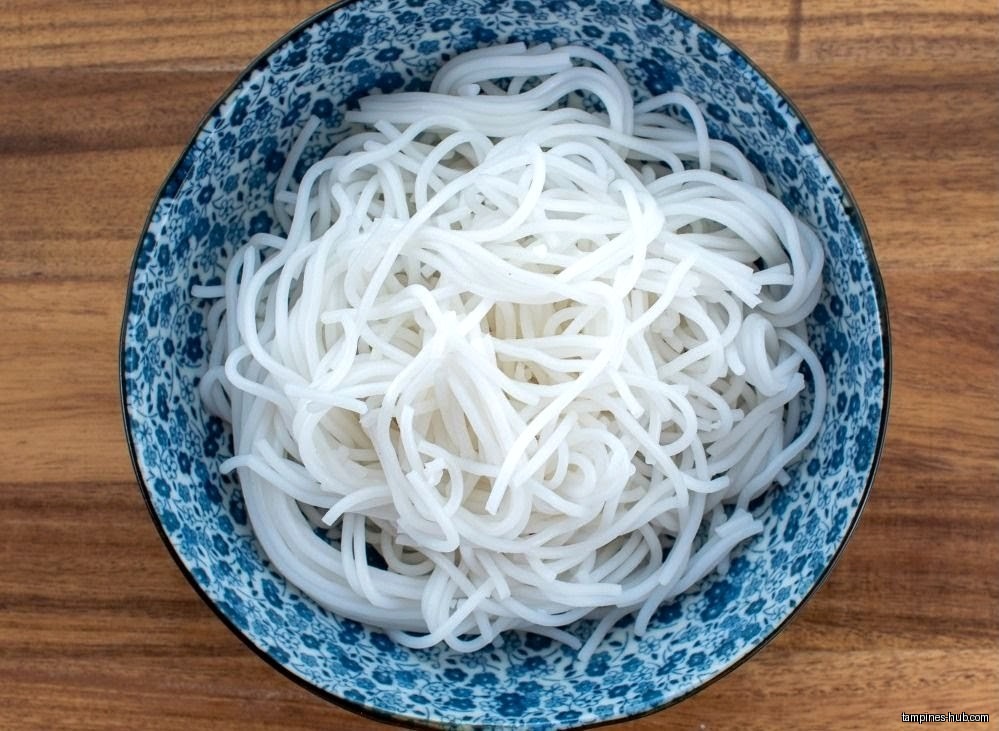 A blue patterned bowl filled with white rice noodles on a wooden surface.
